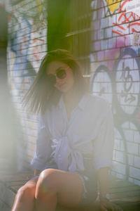 Portrait of young woman sitting on seat against graffiti wall