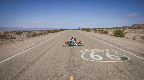 Side view of couple sitting on road against blue sky