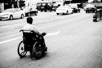 Man in wheelchair on road by cars at city