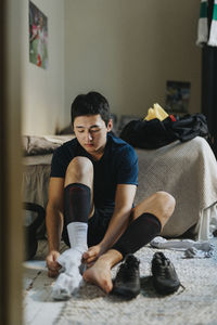 Teenage boy wearing sock while sitting on carpet at home