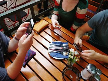 High angle view of friends sitting at table while using mobile phones in restaurant