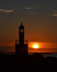 Silhouette lighthouse by sea against sky at sunset