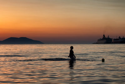Silhouette person in sea against sky during sunset