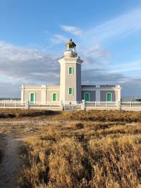 Lighthouse on field by building against sky