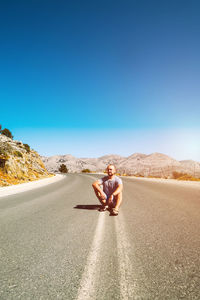 A young man is sitting on a mountain road. the dividing line on the road goes into the horizon. 