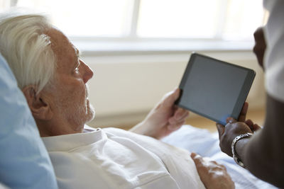 Cropped image of male nurse assisting senior man in using digital tablet at hospital