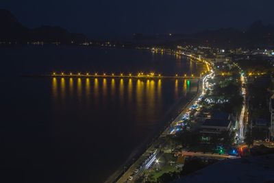 Illuminated city by sea against sky at night