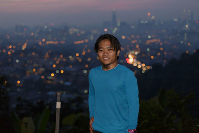 Portrait of smiling man standing against illuminated cityscape at night
