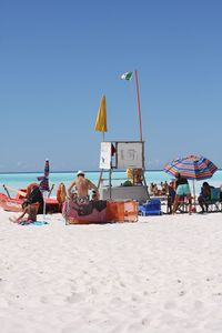 Rear view of people at beach against clear blue sky