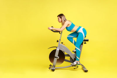Low angle view of young woman exercising against yellow background