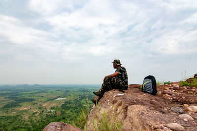 Hiker sitting on rock by mountain against sky