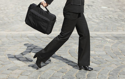 Low section of businesswoman holding bag while walking on city street