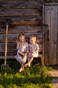 
low angle view of two children reading a book sitting on a wooden bench near an old bathhouse