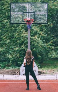 Rear view of woman with arms raised standing against trees