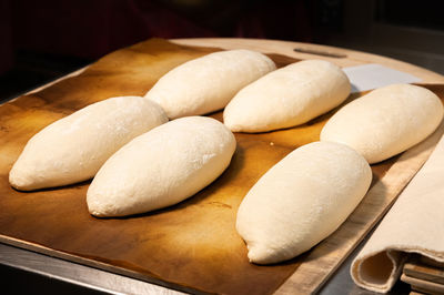 Raw loaves of french bread lying on a wooden tray on a table in a bakery