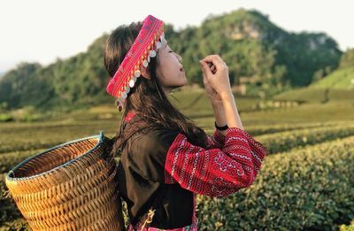 Young woman in traditional clothing carrying basket while standing on agricultural field