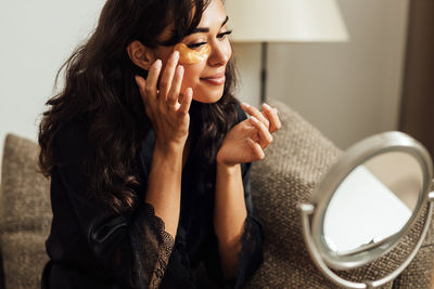 Young woman applying eye patch at home