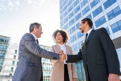 Business colleagues shaking hands while standing against sky