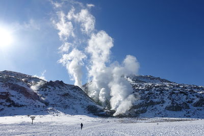 Smoke emitting from snowcapped mountains against sky on sunny day during winter