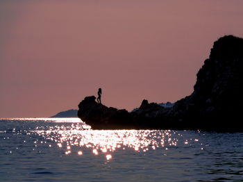 Silhouette person on sea against clear sky during sunset