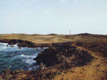 Cliff by sea with light house against sky