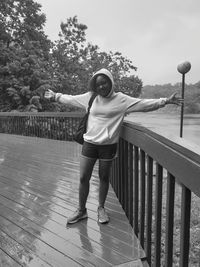 Portrait of young woman standing with arms outstretched by railing