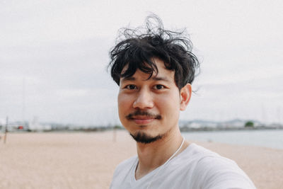 Portrait of young man on beach against sky