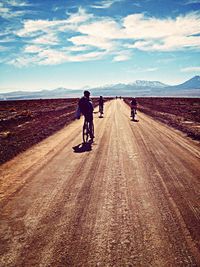 Rear view of people riding bicycle on dirt road