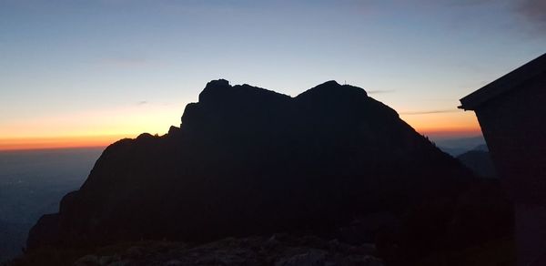 Silhouette rock formation by sea against sky during sunset