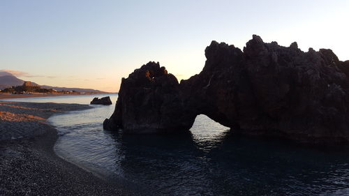 Rock formation on beach against sky during sunset