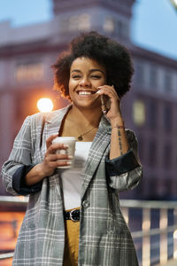 Young woman using smart phone while holding coffee