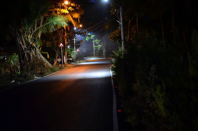 Illuminated road amidst trees at night