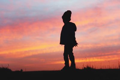 Silhouette of child standing against sunset sky