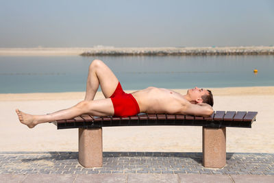 Full length of shirtless man lying on bench outdoors