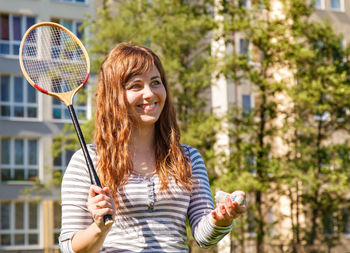 Beautiful young woman playing badminton against building