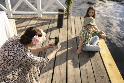 Mother photographing children sitting on jetty