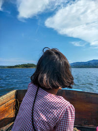 Rear view of woman sitting on boat in sea against blue sky