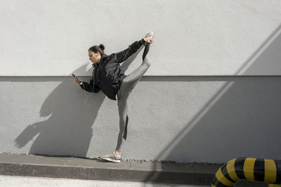 Full length of woman listening music while stretching legs on terrace