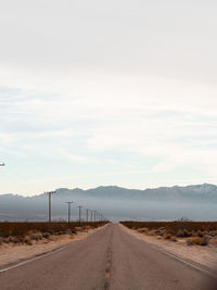 Empty road along landscape against sky