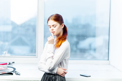 Side view of young woman standing against window