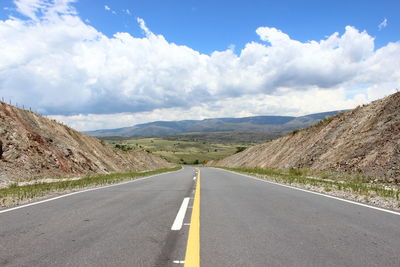 Empty country road amidst mountains against cloudy sky