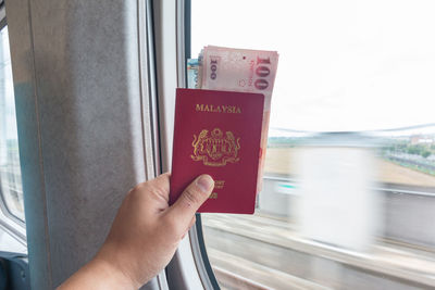 Cropped hand holding malaysian passport with paper currency in train