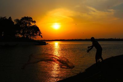 Silhouette man on sea against orange sky during sunset