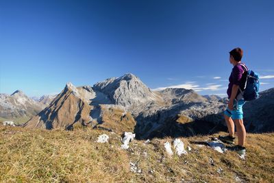 Rear view of man standing on mountain against blue sky