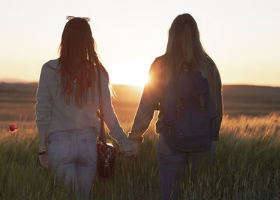 Two women holding hands at sunset in the field