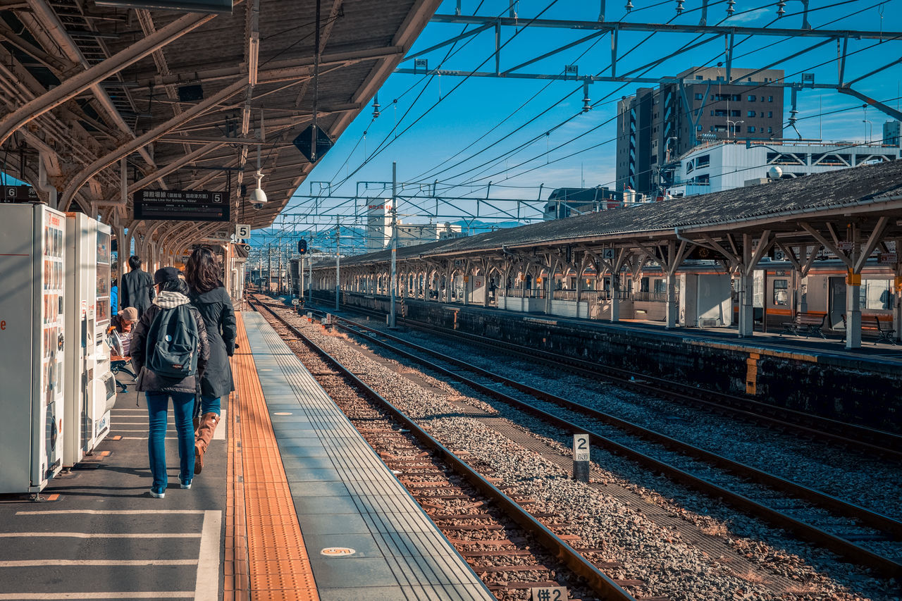 railroad track, transportation, rail transportation, railroad station platform, railroad station, real people, architecture, public transportation, built structure, train - vehicle, lifestyles, men, bridge - man made structure, day, women, full length, outdoors, clear sky, sky, city, one person, people