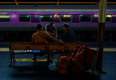 Rear view of people sitting on railroad station platform