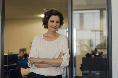 Successful businesswoman leaning in glass door, with arms crossed