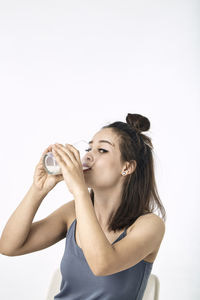 Young woman drinking glass against white background