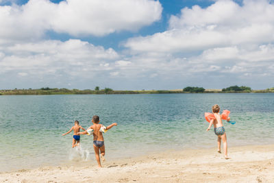 Rear view of shirtless boys running towards sea against cloudy sky